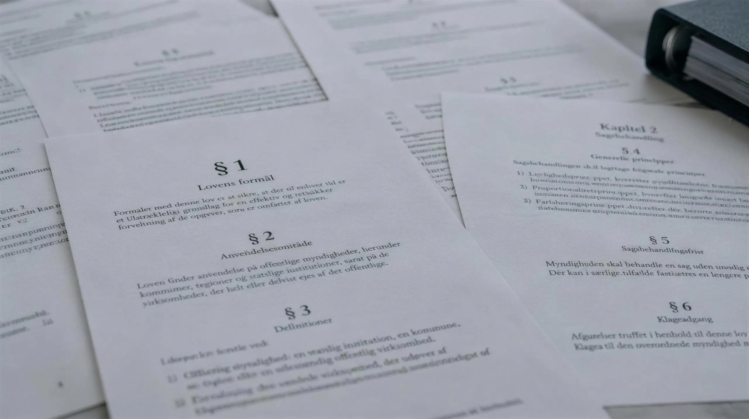 Udskrevne lovsider med paragraffer spredt ud over et bord ved siden af et ringbind